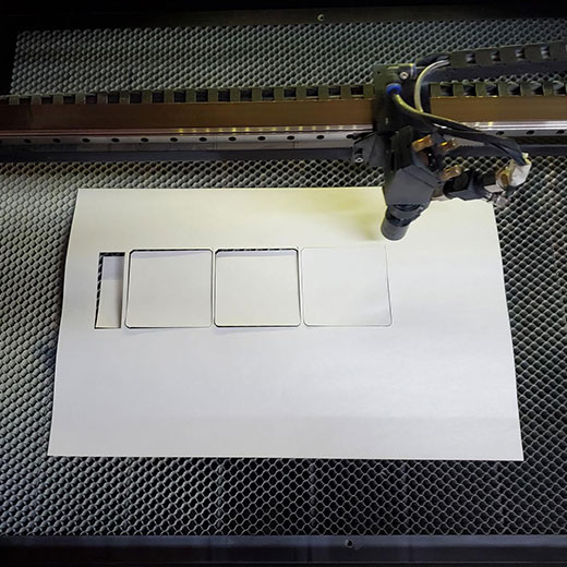 Laser cutter being used to create squares and rectangle cuts into a piece of paper